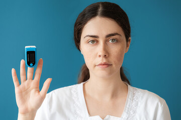 Portrait of woman doctor shows a pulse oximeter on her index finger. Blue background. The concept...