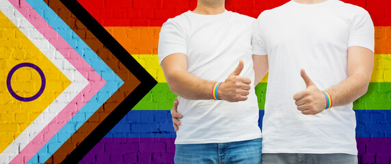 lgbtq, trans and intersex rights concept - close up of male gay couple hugging and showing thumbs...