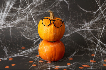 halloween and holiday concept - halloween pumpkins with glasses and spiderweb over dark background