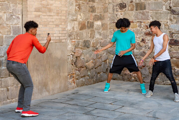 Three afro latin male friends dancing in the street and recording it