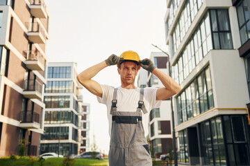 Looking at buildings. Young man working in uniform at construction at daytime
