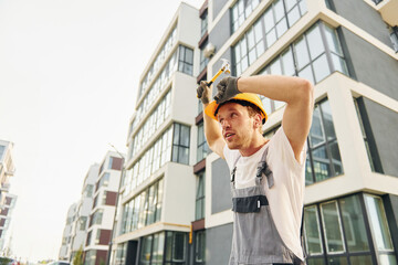 Standing near modern buildings. Young man working in uniform at construction at daytime