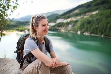 Fototapeta na wymiar Mid adult woman tourist on hiking trip on summer holiday, resting by lake.