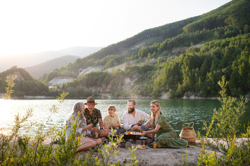 Happy multigeneration family on summer holiday trip, barbecue by lake.