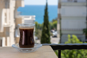 Turkish coffee in transparent traditional glass against buildings and sea view with trees in summer