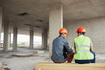 Fototapeta premium Back view at two construction workers wearing hardhats while chatting at construction site, copy space