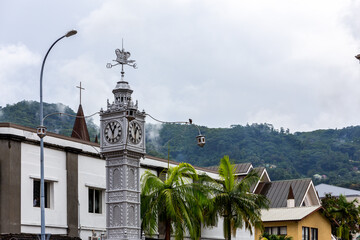 The Victoria Clock Tower, or "mini Big Ben", copy of London's Big Ben in the city center of Victoria, Seychelles' capital, with cloudy sky and palm trees in the background.