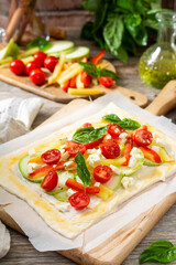 The process of making a puff pastry pie with a vegetable mixture and mozzarella cheese on a serving board on a culinary background closeup. Raw dough and baking ingredients on the table