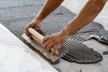 Troweling mortar onto a concrete floor in preparation for laying white floor tile.