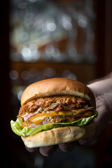 Hand grabbing pulled pork, bacon and cheese burger whith bokeh bacground