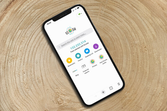BRAUNSCHWEIG, GERMANY - AUGUST 22, 2021: Ecosia internet search engine on cellular phone, placed on tree stump with annual rings. Ecosia plants trees, donation for reforestation. Go green concept.