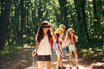 Fototapeta na wymiar Girl standing in front of her friends. Kids strolling in the forest with travel equipment