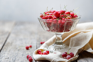 Frozen red currants in a glass vase on a cloth on a rustic wooden table. Close-up.