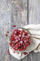 Frozen red currants in a glass vase on a cloth on a rustic wooden table. Close-up.