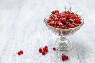 Frozen red currants in a glass vase on a white wooden table. Close-up.