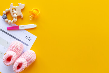Pregnancy test with pink baby girl booties and calendar, top view