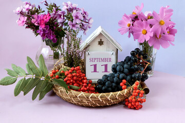 Calendar for September 11 : the name of the month of September in English, cubes with the number 11, autumn flowers and heather branches in bouquets, bunches of rowan and ripe grapes on a tray