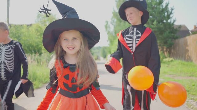 Halloween kids going to collect candy. Trick-or-treating. Guising. Jack-o-lantern. Children in carnival costumes outdoors. Witch and skeletons. Friends with orange balloons. celebrate halloween