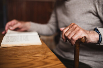 Unrecognizable elderly man sitting at the table indoors at home, reading book.
