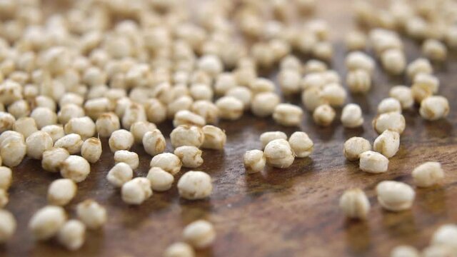 Puffy dry quinoa is scattered on a textured wooden surface in slow motion. Macro shot. Cereal gluten free food concept