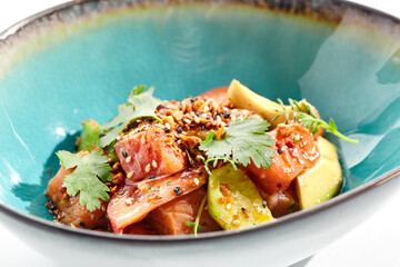 Salmon and avocado salad bowl. Blue salad bowl isolated on white background. Salad garnished with micro greens and sesame, chopped salmon, sliced avocado and parsley green leaf. Raw salmon