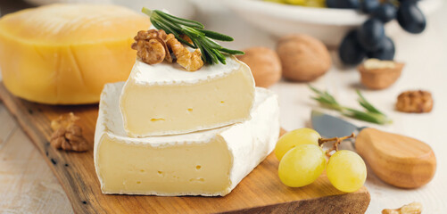 Stack Camembert cheese with grapes, walnuts and basil on gray light concrete or stone background. Selective focus