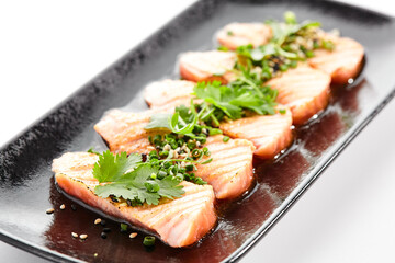 Salmon tataki - seared salmon, thinly sliced sashimi style. Salmon tataki served with delicious citrus ponzu tataki sauce and fresh greens. Japanese seafood on black plate isolated on white