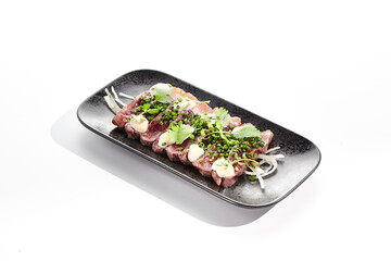 Beef tataki - seared beef,. thinly sliced sashimi style. Beef tataki served with delicious ponzu tataki sauce. Japanese style meat on black plate isolated on white background..
