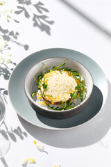 Beef tartare under cheese sauce with deep fried onion. Fancy dinning with beef tartare on white table with simple contemporary decoration. Sunlight and harsh shadow still life. Beef tartare blue dish.