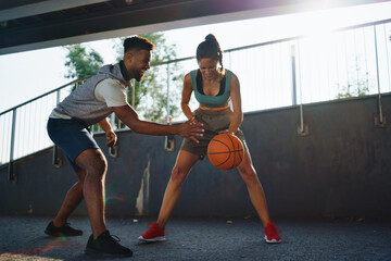 Man and woman friends playing basketball outdoors in city.