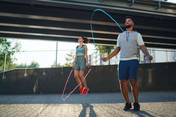 Man and woman couple friends doing workout exercise outdoors in city, skipping.
