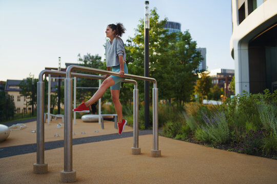 Mid adult woman doing exercise on parallel bars outdoors in city workout park, healthy lifestyle concept.