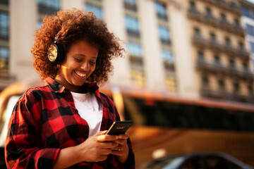 Girl listening to music from her phone. Young woman with curly hair outdoors