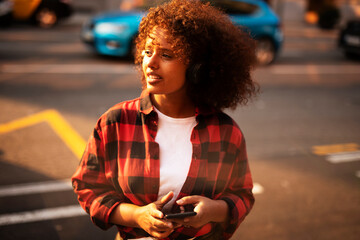 Girl listening to music from her phone. Young woman with curly hair outdoors