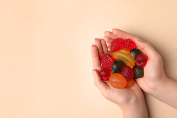 Woman holding pile of delicious gummy fruit shaped candies on beige background, top view. Space for...