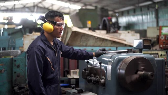 Professional Asian man Industry worker in safety ear muff working in machinery factory. Male labor foreman technician working with metal machine. Manufacturing factory and build construction concept