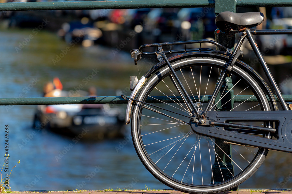 Wall mural selective focus of bicycle back wheel and seat with blurred of canal cruise boat as background, old 