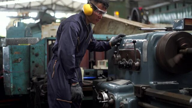 Professional Asian man Industry worker in safety ear muff working in machinery factory. Male labor foreman technician working with metal machine. Manufacturing factory and build construction concept