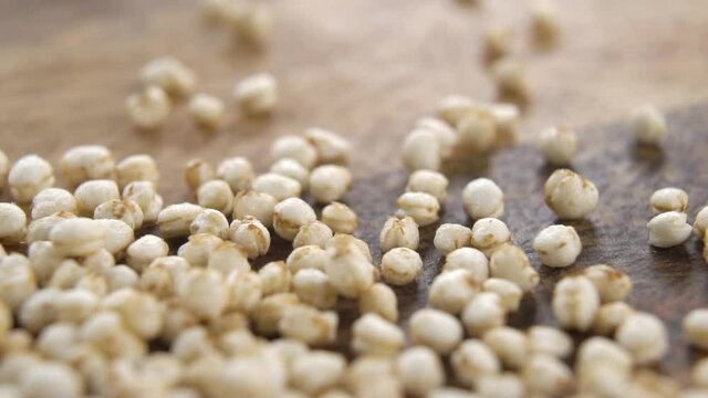 Dry puffy quinoa grains are scattered on a rustic wooden surface. Macro. Gluten free concept. Dolly Shot. Slow motion