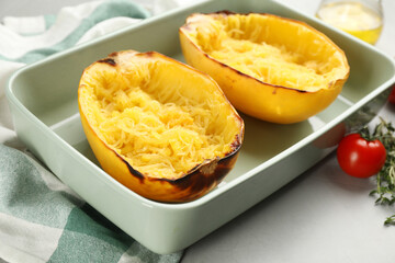Halves of cooked spaghetti squash in baking dish on light grey table, closeup