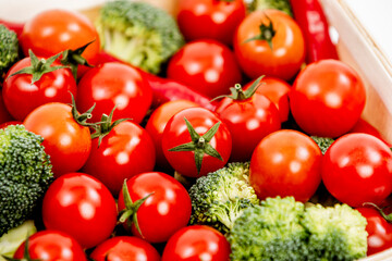 Close-up of bulk ripe cherry tomatoes in a market basket along with broccoli stalks and hot red peppers