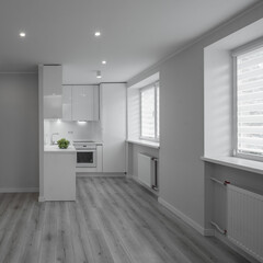 Modern bright interior of luxury studio apartment after renovation. White kitchen with fridge and oven. White walls. Beige parquet.