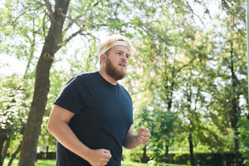 Naklejka na ściany i meble Overweight man in sports clothing running alone in the park