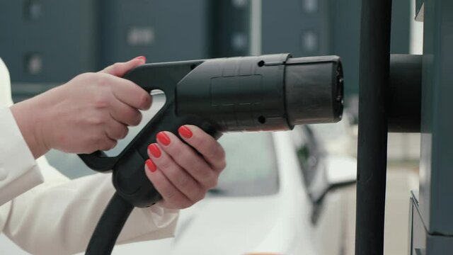 Female hand disconnects DC fast charging socket Japan type from charging station. Business woman holding electric car plug on background of EV. Eco friendly alternative energy concept