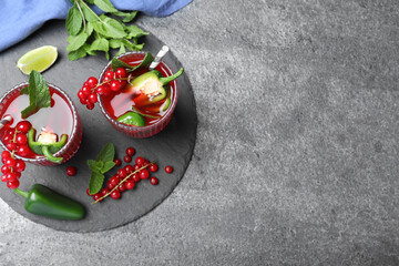 Glasses of spicy red currant cocktail with jalapeno and mint on grey table, flat lay. Space for text