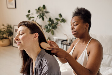 African female brushing hair of her Caucasian girlfriend in the morning