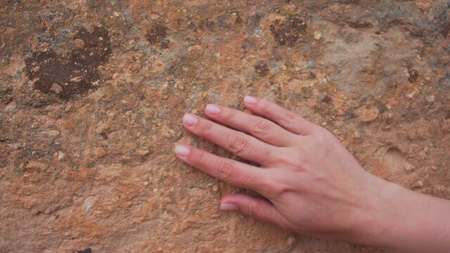 Female hand touching rough weatehred surface of ancient mountain