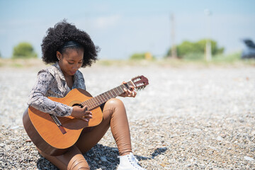 Young woman sitting on a gravel stone ground in the oper air playing her guitar