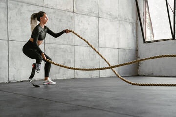 Young sportswoman with prosthesis working out with battle ropes