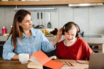 Fototapeta premium White woman helping her daughter with down syndrome using headphones